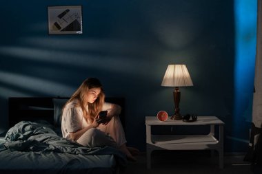 Gece geç saatlerde yatakta cep telefonu kullanan genç bir kadın uykusuzluktan muzdarip, sosyal medya ağında sohbet ediyor. İnternet bağımlılığı kavramı
