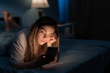 Sosyal medyaya bağımlı genç bir kadın gece yatakta akıllı telefonuyla uyuyakalıyor. Mobil kullanım bağımlılığı kavramı.