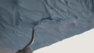 Ressam elinin palet bıçağını kullanarak ressamın elini kapat ve tuval üzerindeki mavi resme doku ekle. Sanat arkaplanı yarat. Dikey video