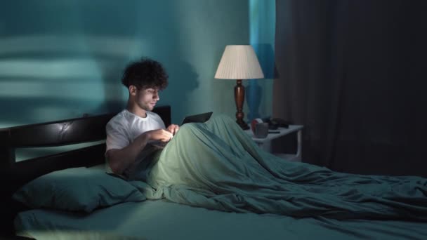 夜までプロジェクトに取り組んでノートパソコンで作業を入力するアラビア語の男性に焦点を当て ノートパソコンとベッドに横たわっていた 若い男のフリーランスのIt開発者が夜コーディング スペースのコピー — ストック動画