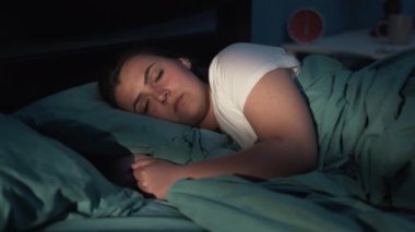 Genç bir kadın geceleri yatak odasında rahat bir şekilde uyuyor. Yakın plan.