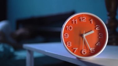 Uyku bozukluğu ya da uykusuzluk konsepti. Saat odak noktasında ve adam yatakta uyumaya çalışıyor. Boşluğu kopyala