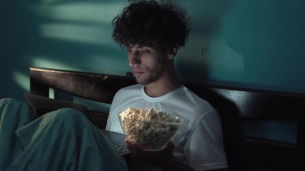 Счастливый Улыбающийся Молодой Человек Ест Попкорн Лежа Кровати Смотрит Кино — стоковое видео