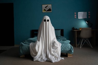Beyaz çarşaflı hayalet geceleri yatak odasında oturur. Korku sahnesi. Cadılar Bayramı konsepti Boşluğu kopyala