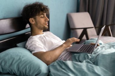 Yatak odasında iş, sosyal ağlar, sörf, internette gezinme. Ciddi bir genç adam uyandı, yatağa oturdu, iç dizüstü bilgisayarda çalışıyor. Boşluğu kopyala