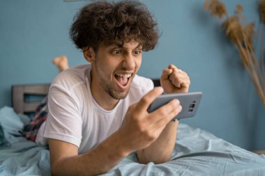 Mutlu oyuncu sabah yatak odasında akıllı telefonuyla video oyunu oynuyor. Esport yayın oyunu çevrimiçi, zafer kazandı