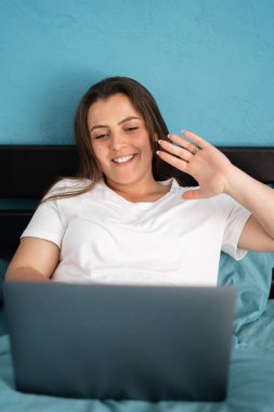 Yatakta oturan genç bir kadın, dizüstü bilgisayarında video görüşmesi yapıyor. Mutlu kız dizüstü bilgisayar ekranına el sallıyor, arkadaşlarıyla ya da aileleriyle konuşuyor. Boşluğu kopyala