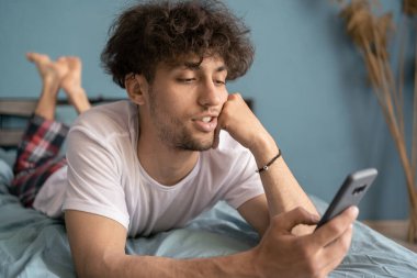 Arap adam yatakta yatarken akıllı telefon kullanıyor, mesajlar okuyor, sosyal ağlarda sohbet ediyor. Mobil aygıtlara bağımlılık kavramı