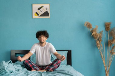 Genç adam yatakta yoga yapıyor, sabah uyanıyor. Meditasyon Konsepti. Boşluğu kopyala