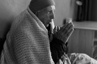 Ekoseye sarılı yaşlı bir adam kendini üşümüş hissediyor. Elini ısıtan emekli bir adam merkezi ısıtmada sorun yaşıyor. Siyah beyaz fotoğraf