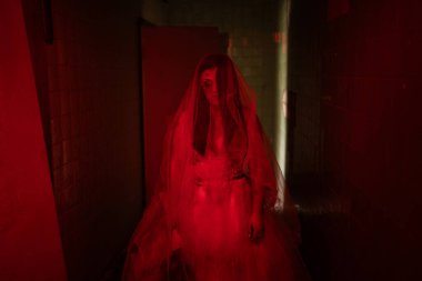 Ölülerin gelini, beyaz elbiseli hayalet bir kadın eski bir binada ya da perili bir evde yürüyor, kırmızı tonlu bir fotoğraf. Boşluğu kopyala