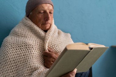 Evdeki ısıtma sorunu yüzünden üşüyen bir adam yatakta oturup kitap okuyor, yakın plan. Isıtma yok kavramı. Boşluğu kopyala