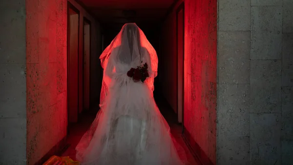 Ghostly figure of woman in wedding dress walking along a creepy hotel in red light. Halloween horror concept
