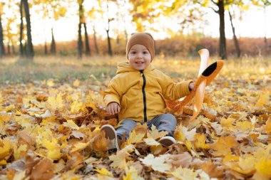 Mutlu çocuk sonbahar parkında düşen yapraklara oturur. Sonbaharda aile açık hava eğlencesi. Copz alanı