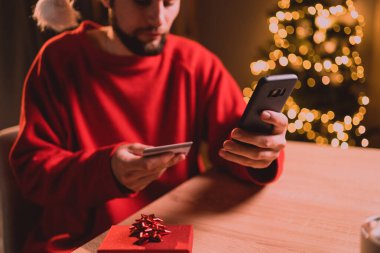 Noel tatilinde online alışveriş. Noel Baba şapkalı adam internet üzerinden akıllı telefon ve kredi kartı kullanıyor. Boşluğu kopyala