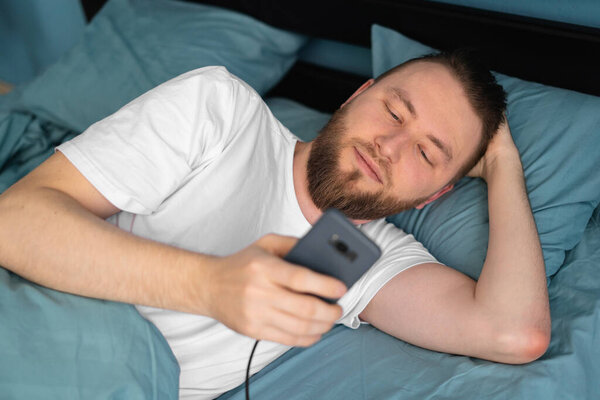 Attractive man using charging smart phone on bed , people and technology concept