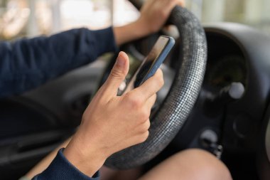 Kadın araba kullanıyor ve akıllı telefon kullanıyor. Araba kullanırken elinde cep telefonuyla mesajlar okuyor. Tehlikeli davranış, kaza riski. Tehlike, suç, gençlik kavramı. Boşluğu kopyala