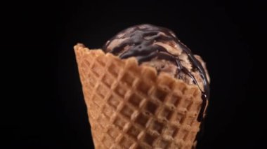 Çikolatalı dondurma, siyah arka planda izole edilmiş waffle külahına çikolata jölesi dökülüyor. Yakın plan.