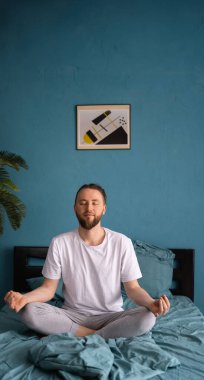 Aydınlık odada yatakta otururken sakallı meditasyon yapan beyaz bir adam. Pankart. Boşluğu kopyala
