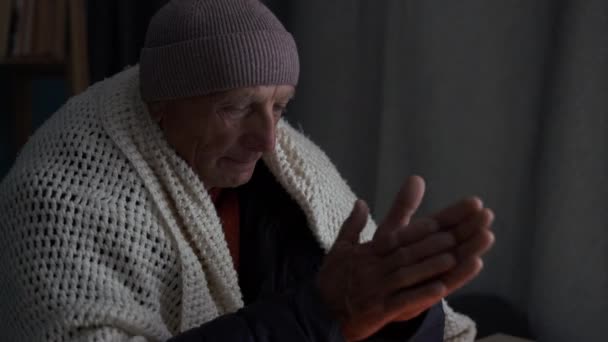 暖かいジャケットの悲しい冷凍老人は 中央暖房なしで寒い部屋のテーブルに座っている燃えるろうそくの上にヤシの木を加熱しようとします スペースのコピー — ストック動画
