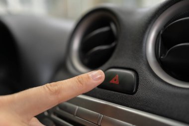 Kadın parmağı arabadaki acil durum ışığı durdurma düğmesine basıyor, kadın kırmızı üçgen tehlike alarmı düğmesine basıyor. Yakın plan.