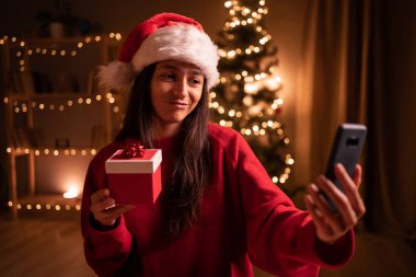Akıllı telefona hediye kutusu gösteren İspanyol kadın tatilini uzaktan kutlarken görüntülü konuşma yapıyor. Boşluğu kopyala