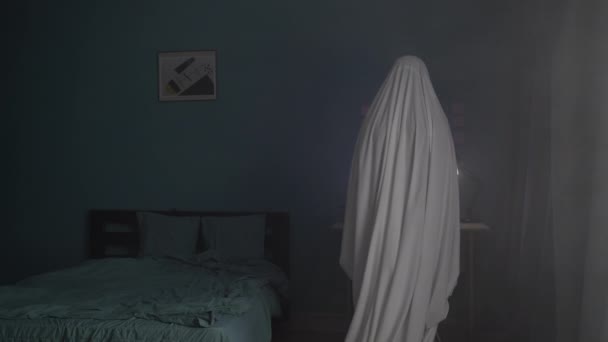 在公寓里的鬼魂 一个被白纸覆盖的男人站在那里看着一张照片 可怕的万圣节的概念 复制空间 — 图库视频影像