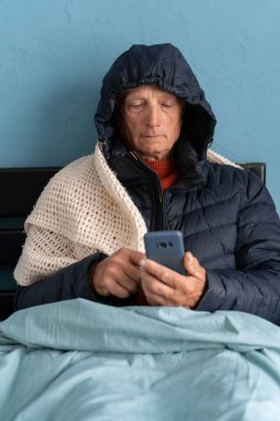 Telefonu olan hasta kıdemli bir adam, battaniyeyle kaplanmış gibi, yatakta oturuyor, evde dondurucu soğuktan titriyor, merkezi ısıtma yok, problem yok ve grip konsepti yok. Boşluğu kopyala