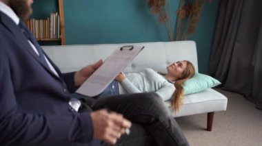 Psikolojik travma konsepti. Ofiste depresyonda olan genç bir kadınla çalışan profesyonel psikolog terapistle seans yaparken kanepede yatan kadın hasta. Boşluğu kopyala