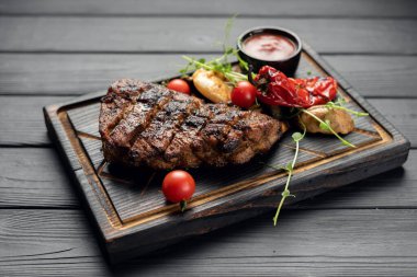 Barbekü 'den alınmış ızgara domuz bifteği. Yanında acı biber ve kiraz domatesleri eski bir ahşap kesim tahtasının üzerinde servis ediliyor. en üstteki görünüm