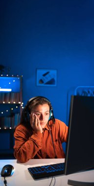Geceleri neon ışıkta evde otururken çevrimiçi video oyunları oynayan yorgun bir oyuncu. Dikey afiş. Boşluğu kopyala