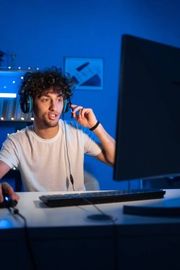 Olumlu Arap oyuncu oyunu bilgisayarda yayınlıyor ve kameraya gülümsüyor. Gülümseyen oyuncu video oyunları oynuyor. Boşluğu kopyala