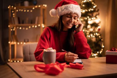 Noel Baba şapkalı bir serbest çalışan telefon görüşmelerine cevap veren ve evde Noel gecesi uzaktan kumandalı bir proje üzerinde çalışırken deftere yazan bir kadın. Boşluğu kopyala