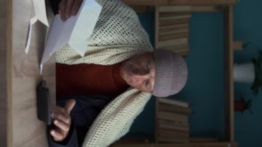 Elektrik, gaz ve ısıtma faturalarını elinde tutan yaşlı bir adamı dondurmak, hesap makinesinin masraflarını hesaplamak. Küresel enerji krizi kavramı. Soğuk ev. Dikey video
