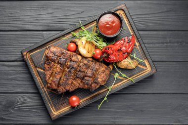 Koyu arkaplanda ızgara domuz pirzolası, kiraz domatesleri, biber ve barbekü sosuyla servis edilir. Üst görünüm, alanı kopyala