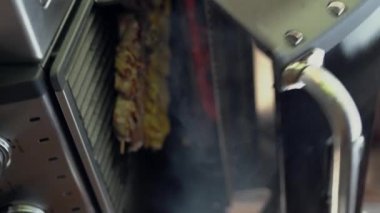 Adam yazın açık havada ızgarada kebap pişiriyor, elleri yakın. Dikey video
