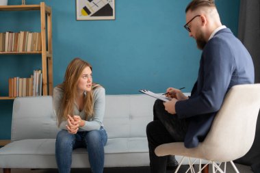 Psikolog, ofisinde üzgün genç bir bayanla terapi seansı sırasında notlar alıyor. Boşluğu kopyala