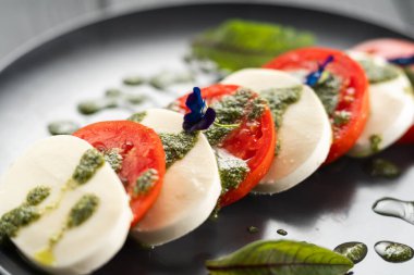 Dilimlenmiş domatesli İtalyan caprese salatası, mozzarella, fesleğen ve siyah arka planda zeytinyağı. Yan görüş. Yakın plan.