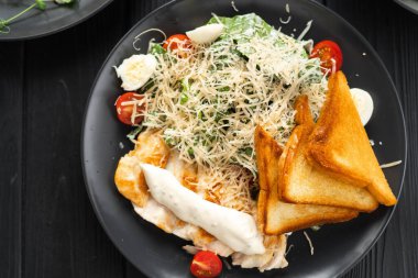 Geleneksel Sezar salatası. Izgara tavuk, domates, peynir ve siyah arka planda kızarmış ekmek. Üst Manzara. Boşluğu kopyala