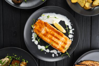 Siyah ahşap masada limonlu ve kremalı kızarmış somon bifteği, üst manzara, düz yatak. Boşluğu kopyala