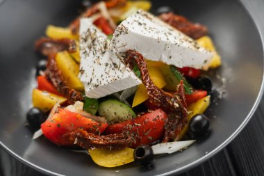 Taze sebzeli Yunan salatası, zeytin ve peynir, siyah tabakta zeytin yağı, üst manzara, koyu arka plan. Geleneksel Yunan mutfak salatası. Yakın plan.