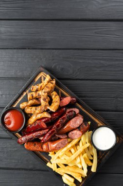 Koyu ahşap arka planda patates kızartması ve sosla servis edilen ızgara soslar, üst manzara. Uzayı kopyala Dikey pankart