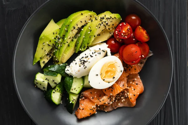 大麻哈鱼 鸡蛋和新鲜蔬菜早餐的关键饮食部分放在黑色木制桌子上的盘子里 Keto饮食食物概念 — 图库照片