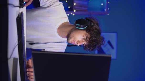 青いネオンで彼のコンピュータ上でオンラインビデオゲームをプレイするプロのアラビア人ゲーマーは部屋にライトを導いた オンラインゲームをプレイするヘッドフォンを身に着けている衝撃的なストリーマープロゲーマー 垂直ビデオ — ストック動画