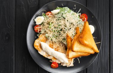 Geleneksel Sezar salatası. Izgara tavuk, domates, peynir ve siyah arka planda kızarmış ekmek. Üst Manzara. Boşluğu kopyala