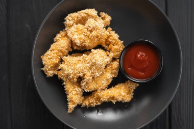 Koyu ahşap arka planda siyah bir tabakta kızarmış tavuk göğsü külçelerinin üst görüntüsü.