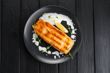 Koyu ahşap zemin üzerinde kremalı sos serpiştirilmiş limon dilimli taze ızgara somon. Boşluğu kopyala