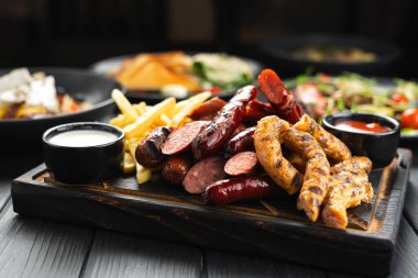 Izgara sosis, fırında patates ve koyu ahşap arka planda hazırlanmış hazır mezeler. Yakın plan.