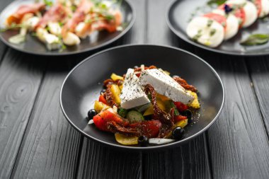 Klasik Yunan domates salatası, salatalık, kırmızı biber, zeytinli soğan, kurutulmuş domates, kekik peyniri ve ahşap bir masada akşam yemeği için diğer tabaklar. Boşluğu kopyala