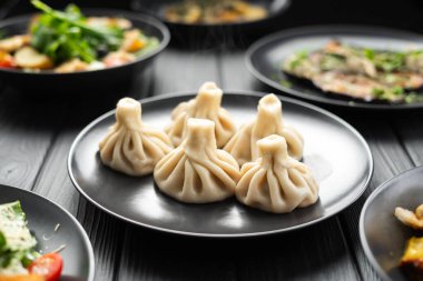 Siyah ahşap masada Gürcü mutfağı. Geleneksel Gürcü mutfağı ve yiyeceği. Khinkali ve bir tabak daha. Boşluğu kopyala